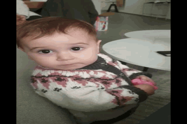 a baby in a pink and white sweater is laying on the floor