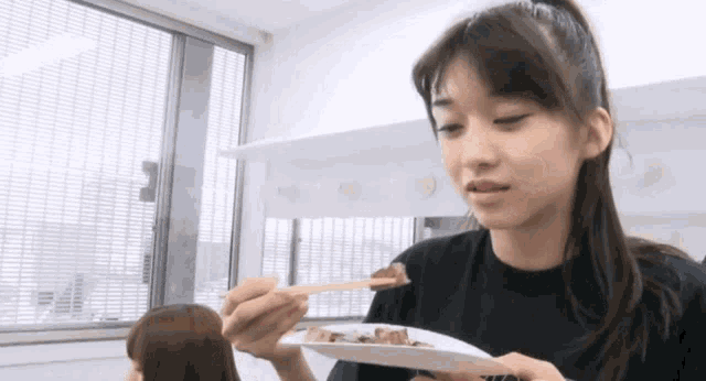 a woman is holding a plate of food with chopsticks .
