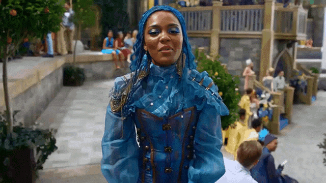 a woman with blue hair and a blue dress is standing in front of a crowd of people .