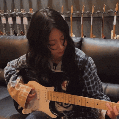 a woman is playing a guitar in front of a row of guitars