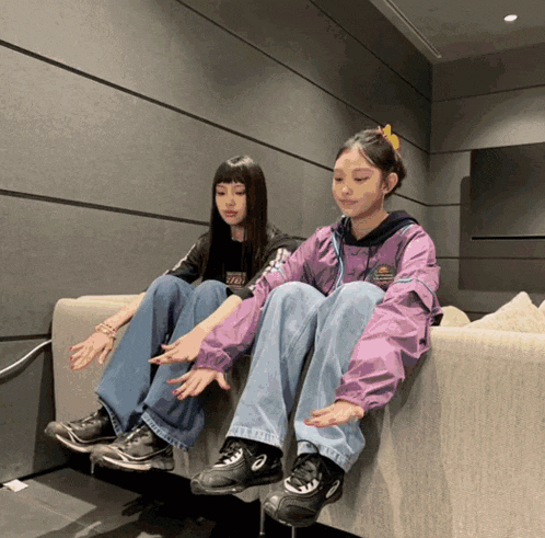 two girls are sitting on a couch with one wearing a jacket that says ' tokyo ' on the front