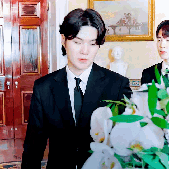a man in a suit and tie is standing in front of a bouquet of white flowers .