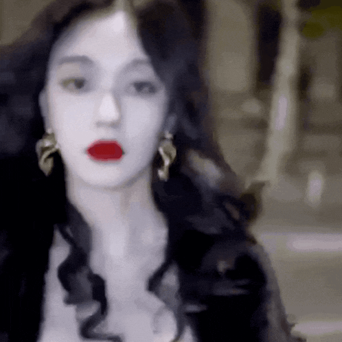 a woman with long black hair and red lips is wearing a black jacket and earrings .