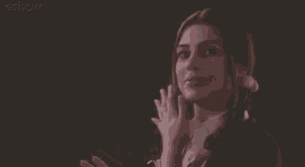 a woman is smiling and clapping her hands in front of a black background .