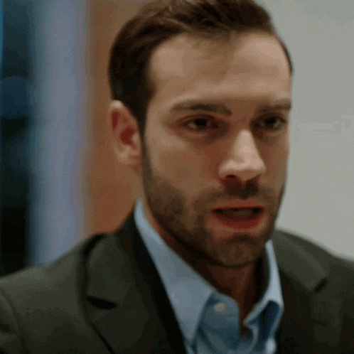 a man with a beard wearing a suit and a blue shirt looks surprised