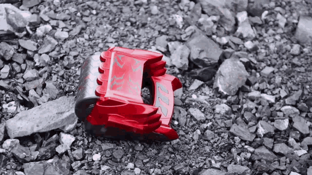 a red toy car is laying on a rocky surface