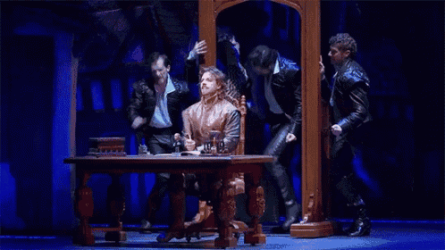 a group of men are standing around a table with one man sitting at it