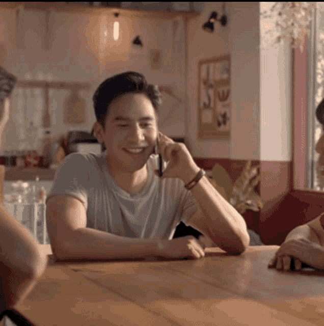 a man sits at a table talking on a cell phone and smiling