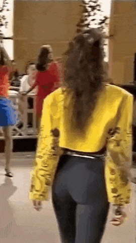 a woman in a yellow jacket and black pants is standing in front of a group of women .