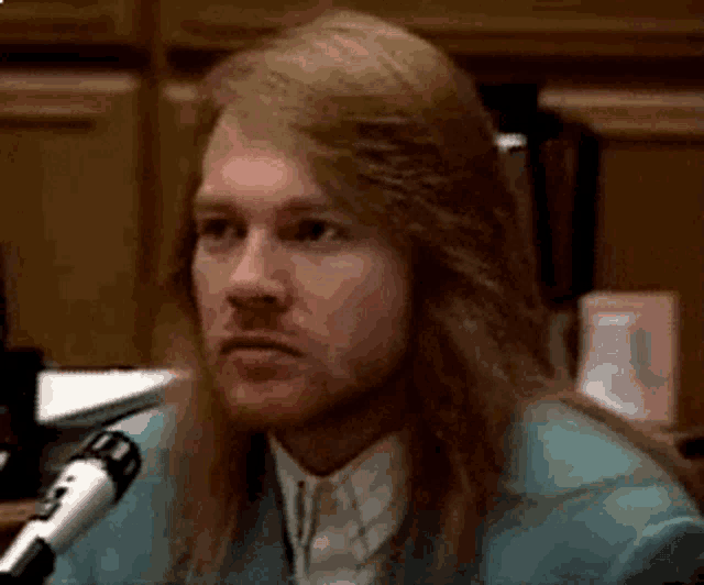 a man with long hair and a beard is sitting in front of a microphone in a courtroom .