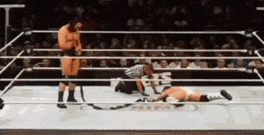 a wrestler is laying on the ground in a wrestling ring while a referee looks on
