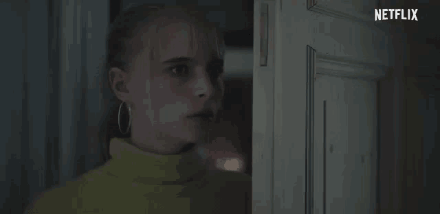 a woman in a yellow turtleneck is standing in front of a door that says netflix