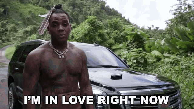 a shirtless man is standing in front of a car and says i 'm in love right now .