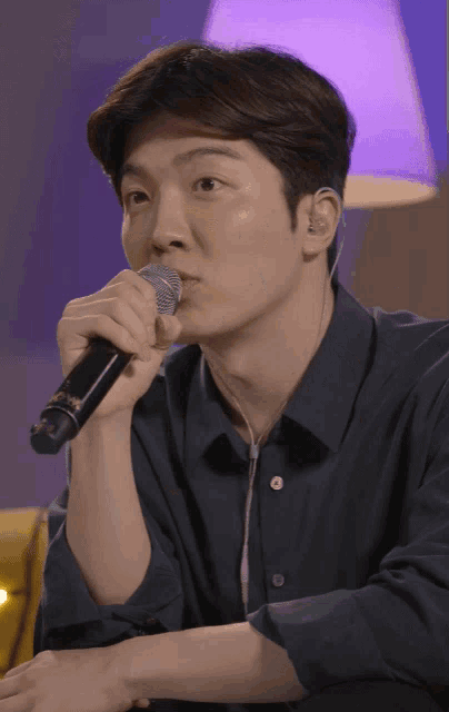a man singing into a microphone with a purple light behind him