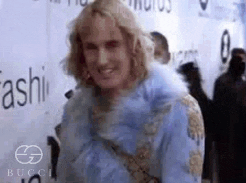 a man is standing on a red carpet wearing a blue fur coat and smiling .