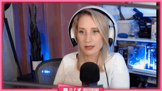 a woman wearing headphones talks into a microphone in front of a pink geekbomb banner