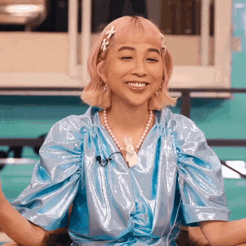 a woman with pink hair wearing a blue top and pearls