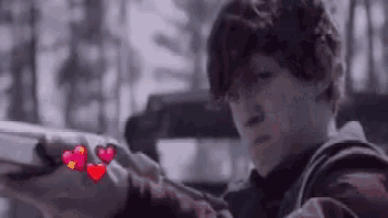 a young boy is sitting in a car with a gun and a heart on his arm .