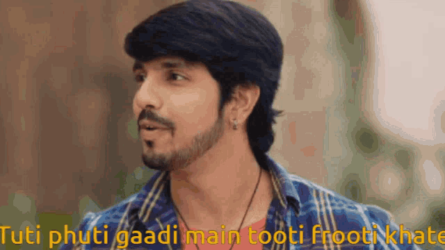 a man with a beard and a plaid shirt says " tuti phuti gaadi main tooti froot khate "