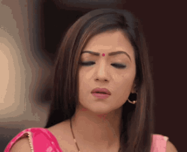 a woman in a pink saree with a red dot on her forehead .