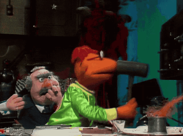 two muppets are sitting at a table and one of them is drinking from a cup