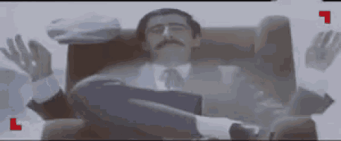 a man in a suit and tie is sitting in a chair with his hands in the air .