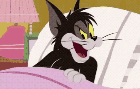 a cartoon cat is laying in a bed with his mouth open and smiling .