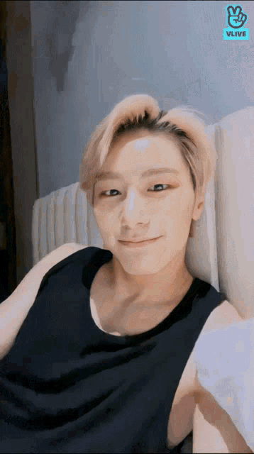 a man in a black tank top is laying on a bed with vlive on the bottom right