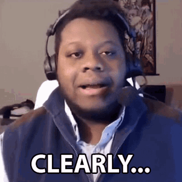 a man wearing headphones and a vest is talking into a microphone and saying clearly .