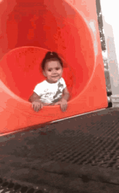 a little girl in a white shirt is playing on a red slide