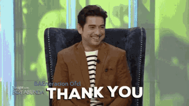 a man in a suit is sitting in a chair and smiling with the words thank you above him