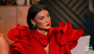 a woman in a red dress with ruffled sleeves is sitting on a chair .
