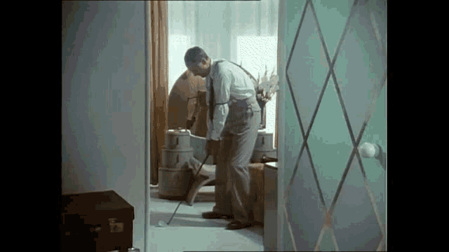 a man is cleaning the floor with a vacuum cleaner and a golf club