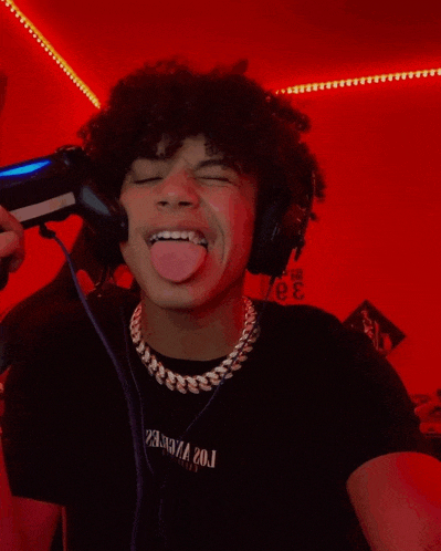 a young man wearing headphones and a black shirt that says los angeles sticking out his tongue