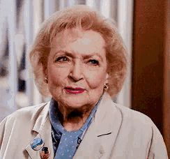 a close up of an older woman wearing a white jacket and a blue shirt