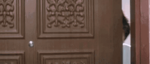 a man is peeking out of a door and smiling at the camera .