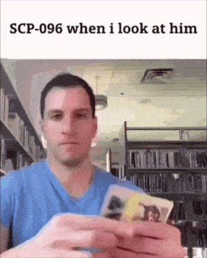 a man in a blue shirt is holding a stack of cards in front of a bookshelf .