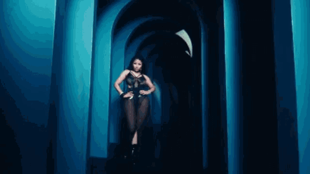 a woman in a black bodysuit is walking through a tunnel of blue arches .