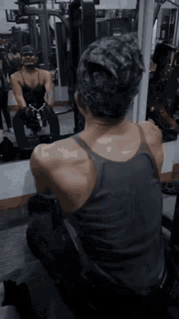 a man is sitting on a machine in a gym while looking at himself in the mirror .