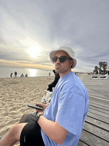 a man wearing a hat and sunglasses is sitting on a beach