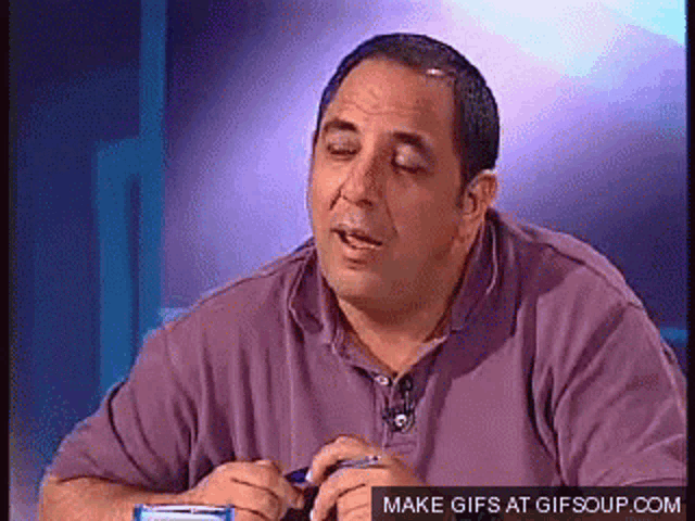 a man in a purple shirt is sitting at a table with a make gifs at gifsoup.com icon
