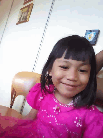 a little girl wearing a pink dress is smiling for the camera