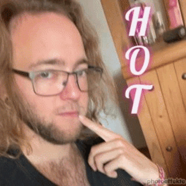 a man wearing glasses and a black shirt has his finger on his lips and the word hot is above him