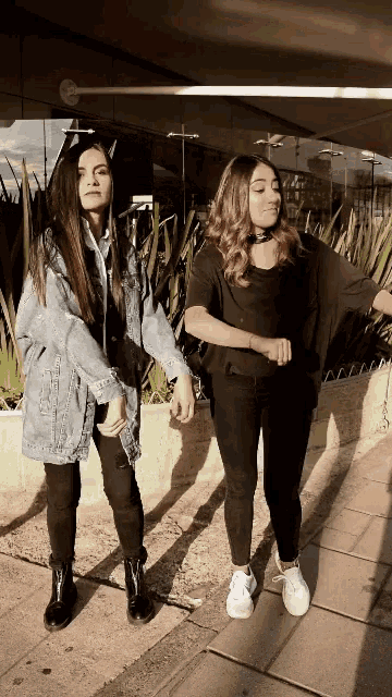 two girls are holding hands and dancing on a sidewalk