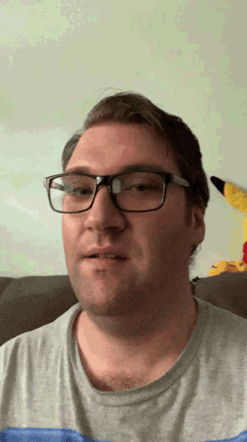 a man wearing glasses and a gray shirt is sitting on a couch
