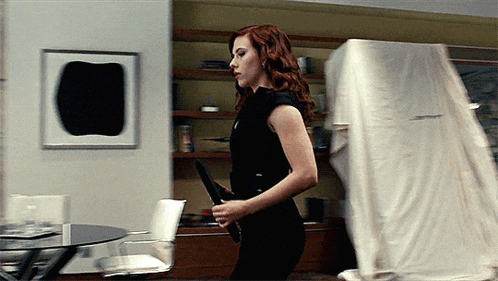 a woman in a black dress is holding a gun in a living room