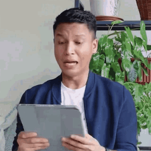 a man in a blue jacket is holding a tablet in his hands .