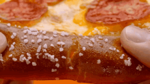someone is holding a pretzel in front of a pizza