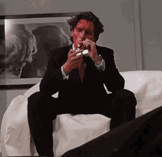 a man in a suit is smoking a cigarette while sitting on a couch .
