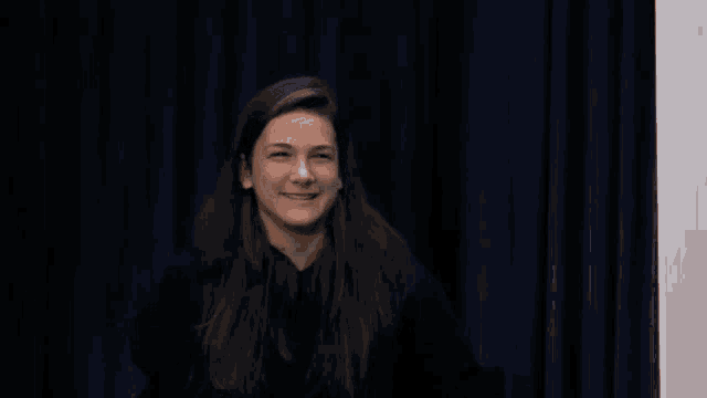 a woman in front of a blue curtain smiles
